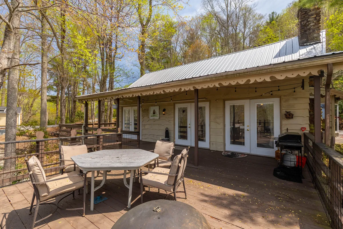 This image features a spacious wooden deck nestled among towering trees, complete with an outdoor dining table and double doors leading directly inside. The scene is bathed in natural light, offering a sense of seamless indoor/outdoor living and highlighting the deck's accessibility from the main living spaces.