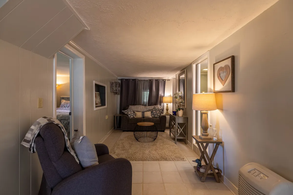 A cozy living space featuring a plush sofa, soft area rug, decorative lamp, and wall art. The intimate lighting and furnishings invite guests to unwind and socialize or enjoy quiet moments alone.