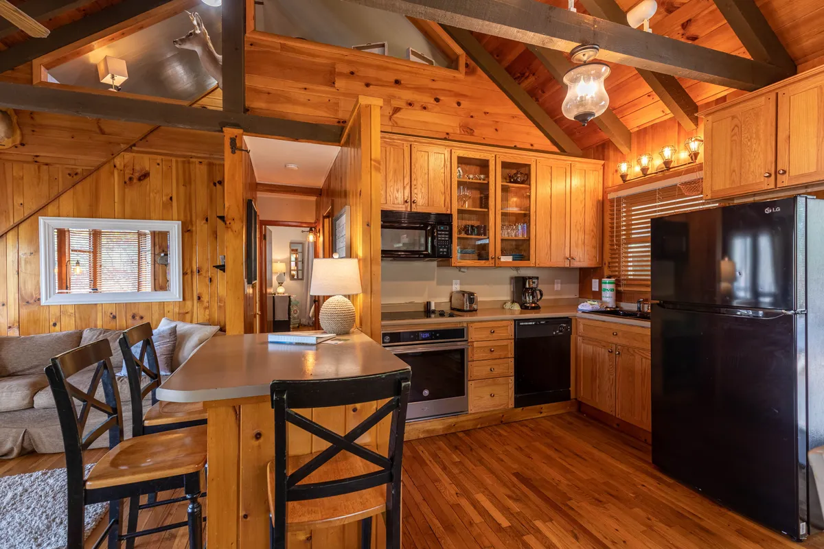 A closer look at the kitchen area, featuring a central island with bar stools, stylish wooden cabinetry, and modern black appliances. The layout encourages shared cooking experiences and casual conversation, with inviting lighting and a warm, sociable atmosphere.