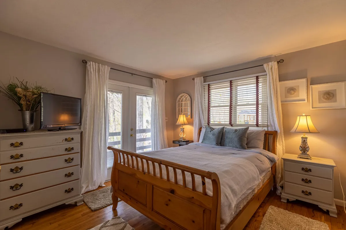 A tranquil bedroom with a full-size bed, a dresser, mirrored wall decor, and a soft lamp. Warm, neutral tones create an inviting atmosphere perfect for restful sleep or quiet relaxation. The setup is practical yet inviting, echoing the suite's promise of comfort and independence.