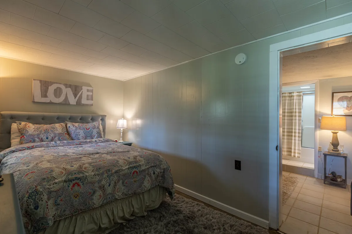 An inviting bedroom featuring a bed with colorful bedding and a decorative 'LOVE' sign above, bathed in a warm glow from a bedside lamp. The atmosphere is intimate and welcoming, perfect for couples seeking a special retreat.
